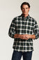 A man wearing a long-sleeve button-down plaid shirt in green, white, and yellow, paired with dark blue jeans, photographed against a light gray studio background.