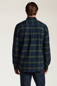 A man viewed from the back wearing a dark navy and green plaid flannel shirt with blue jeans, set against a plain light gray studio background.