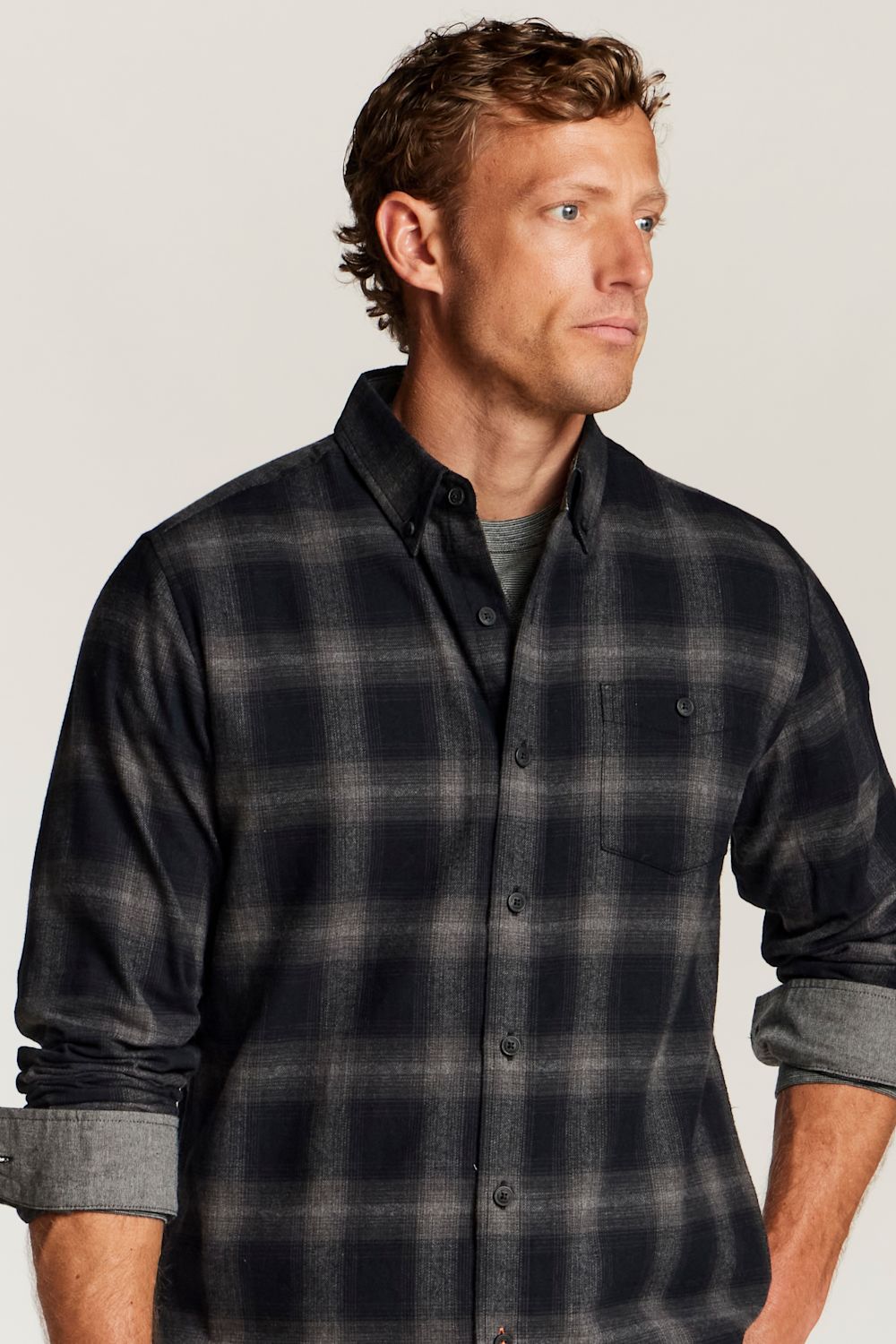 A man wearing a dark navy and gray plaid button-down flannel shirt over a gray t-shirt, photographed against a solid light gray background.