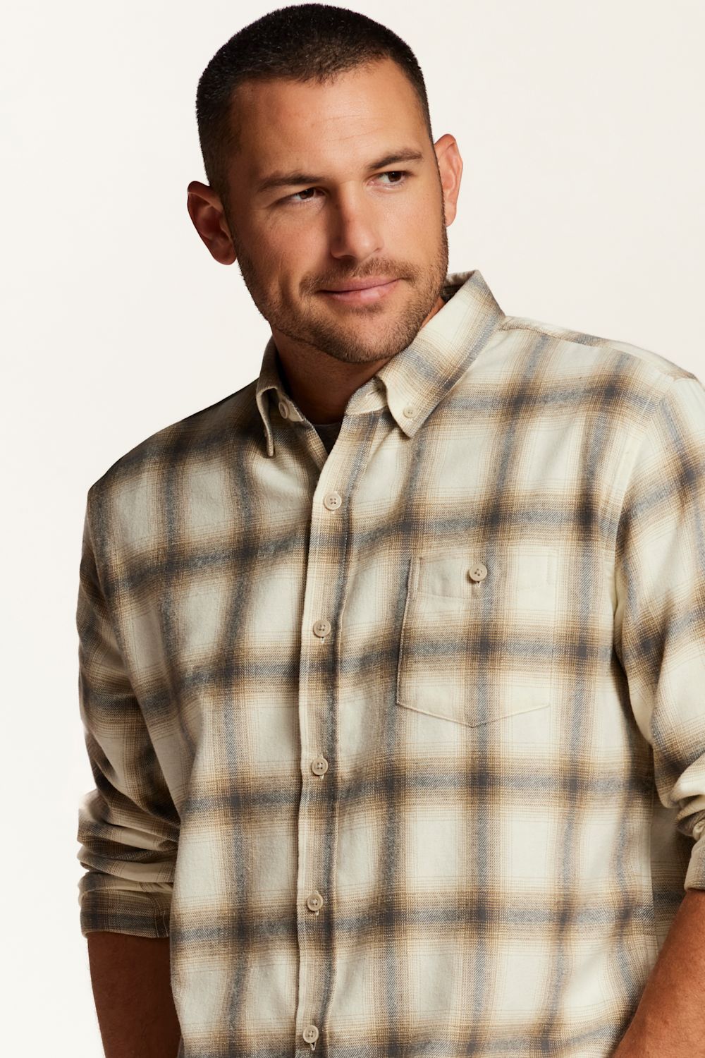 A man wearing a beige and brown plaid button-down shirt, photographed from the chest up against a plain light background.