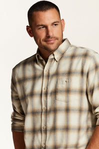 A man wearing a beige and brown plaid button-down shirt, photographed from the chest up against a plain light background.