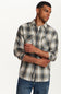 A man wearing a long-sleeve plaid button-up shirt in gray, white, and black, paired with blue jeans, photographed against a clean white studio background.