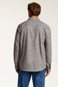 A man viewed from behind wearing a gray textured long-sleeve button-up shirt and blue jeans against a plain white studio background.