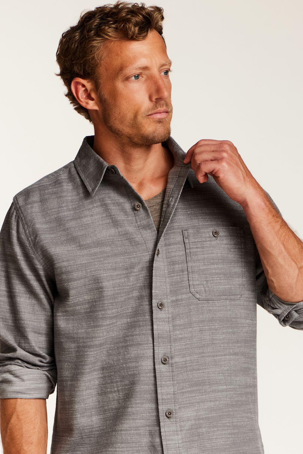 A man wearing a gray textured long-sleeve button-down shirt with a chest pocket, shown from the chest up against a plain light background.