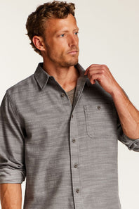 A man wearing a gray textured long-sleeve button-down shirt with a chest pocket, shown from the chest up against a plain light background.