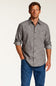 A man wearing a gray long-sleeve button-down shirt with rolled-up sleeves and blue jeans, standing against a plain light background.
