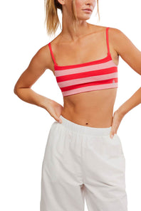 FP Movement Tighten Up Reversible Bra for Women in Grapefruit Combo; Woman wearing a red and pink striped sports bra with white pants on a white background