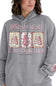 A woman wearing a heather gray pullover hoodie with a festive Christmas graphic on the front. The graphic features the words 'FARM TO FRESH' and 'CHRISTMAS TREE' in pink script, with three vertical panels showing decorated Christmas trees and a pink ornament.