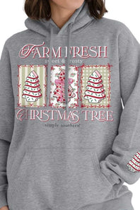 A person wearing a heather gray pullover hoodie with a Christmas tree graphic on the front. The graphic features the text 'FARM FRESH' and 'CHRISTMAS TREE' with three illustrated trees in red, pink, and green on cream panels.