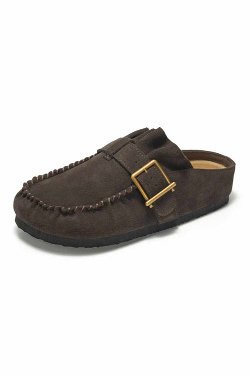 A dark brown suede moccasin-style clog shoe with a decorative strap and a gold-tone buckle, shown from a side angle on a white background.