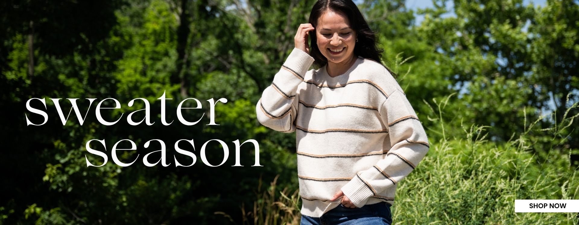 A promotional banner featuring a woman standing in an outdoor green forest area wearing a cream sweater with tan and black stripes. The text on the left side of the image reads SWEATER SEASON and the bottom right hand corner has a white rectangular box with SHOP NOW text