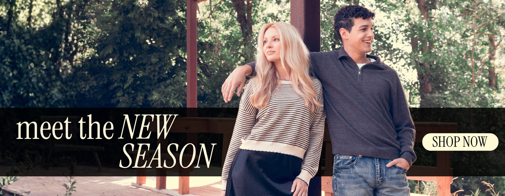 Promotional banner featuring two models standing outdoors in fall outfits. One wears a striped knit sweater and black skirt, while the other wears a charcoal quarter-zip sweater and jeans. A black overlay reads, "Meet the New Season," with a "Shop Now" button.