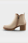 A beige ankle boot with a side zipper, low block heel, and chunky lug sole, shown from a side profile on a light gray background.