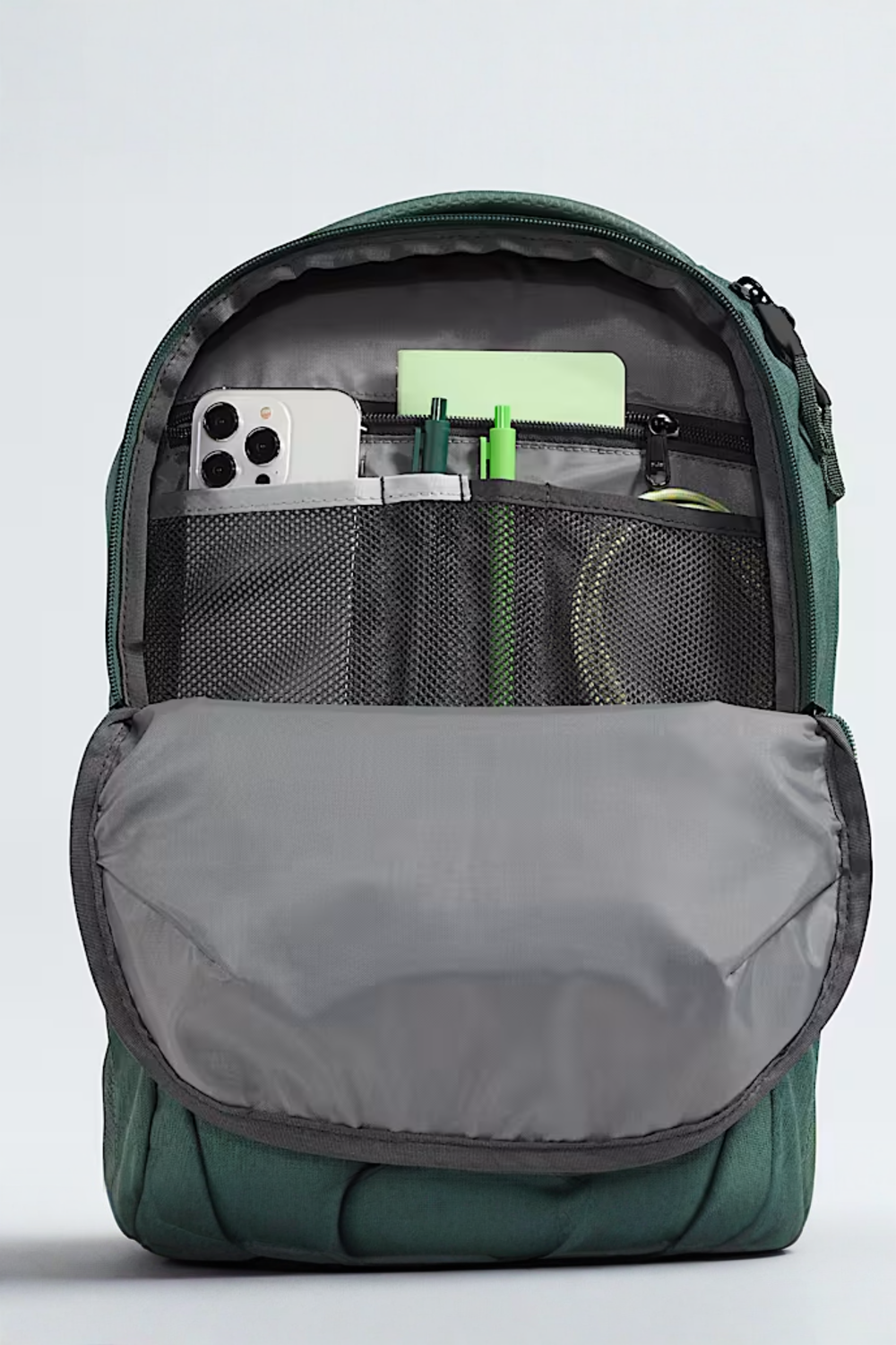 Green backpack with compartments containing electronic devices and stationery on a light gray background