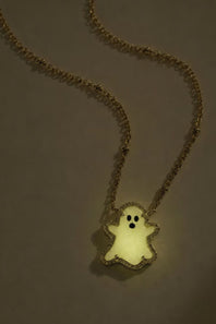A gold chain necklace with a glowing, ghost-shaped pendant, photographed against a dark gray background.
