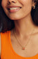 A close-up lifestyle shot of a woman wearing a delicate gold chain necklace with a small pumpkin oval pendant, paired with a bright orange ribbed tank top.