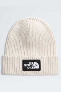 An off-white ribbed knit beanie hat featuring a black rectangular patch on the front with the white 'THE NORTH FACE' logo.