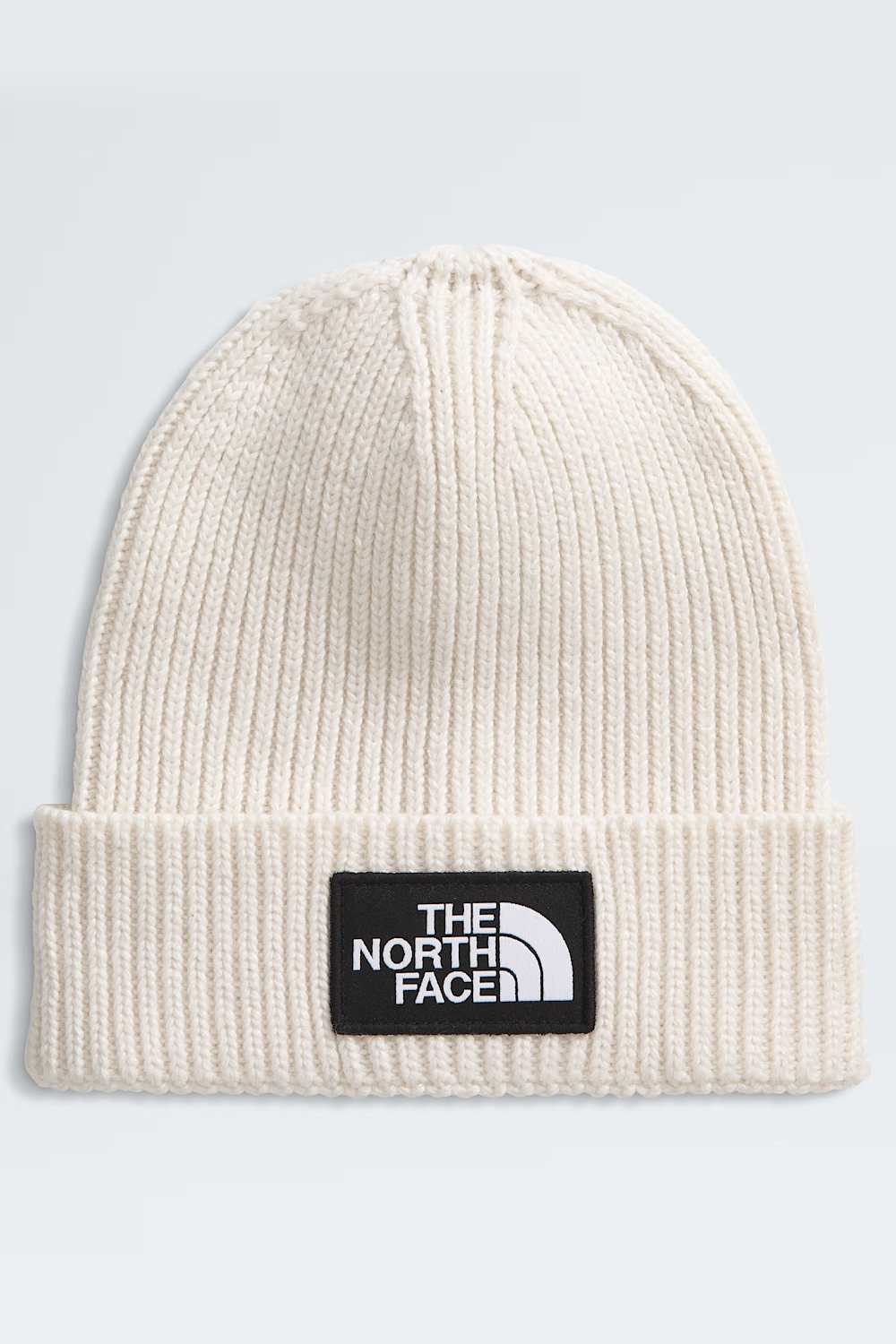 An off-white ribbed knit beanie hat featuring a black rectangular patch on the front with the white 'THE NORTH FACE' logo.