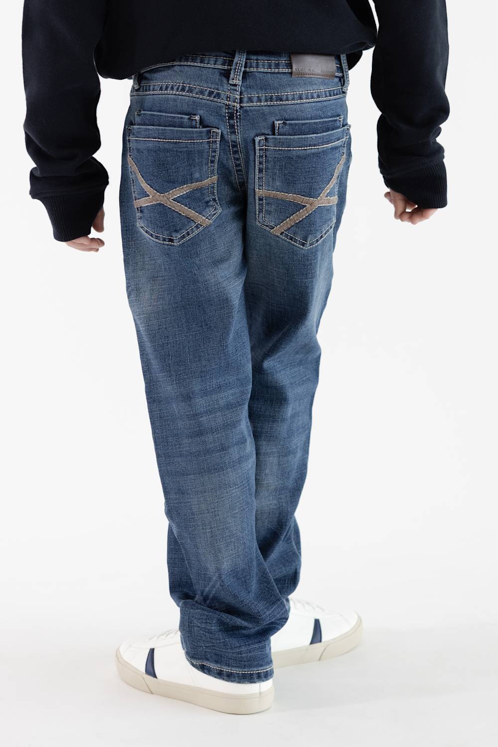 Rear view of a boy wearing Axel Jeans medium-wash straight-leg denim featuring cross-stitched tan embroidery on the back pockets, styled with white sneakers.