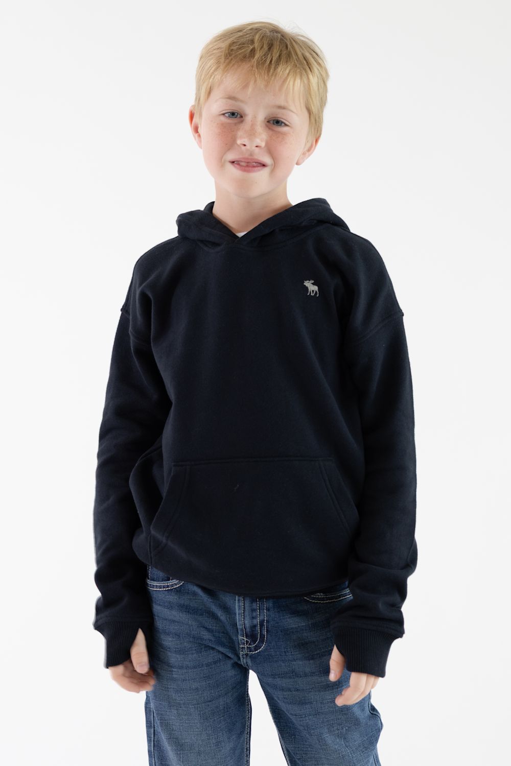 A young boy with blonde hair wearing a dark navy blue hooded sweatshirt with a small embroidered moose logo on the left chest, paired with blue jeans, standing against a plain white studio background.