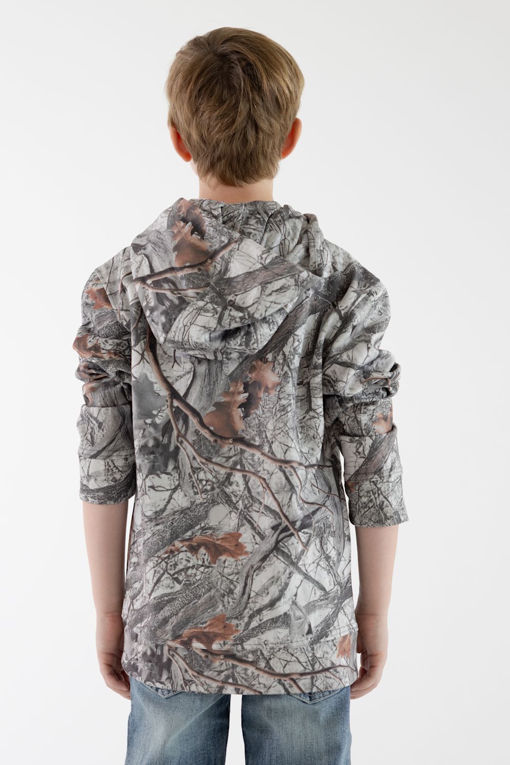 Back view of a young boy facing away from the camera, wearing a long-sleeve hooded camouflage sweatshirt in Woods Print Camo paired with blue jeans against a solid white background.