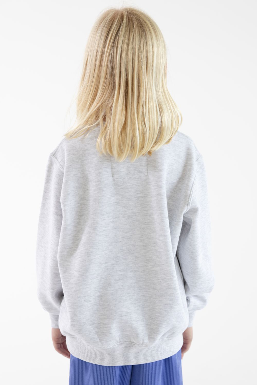 A child with blonde hair seen from the back, wearing a light heather gray sweatshirt and blue pants against a plain white background.