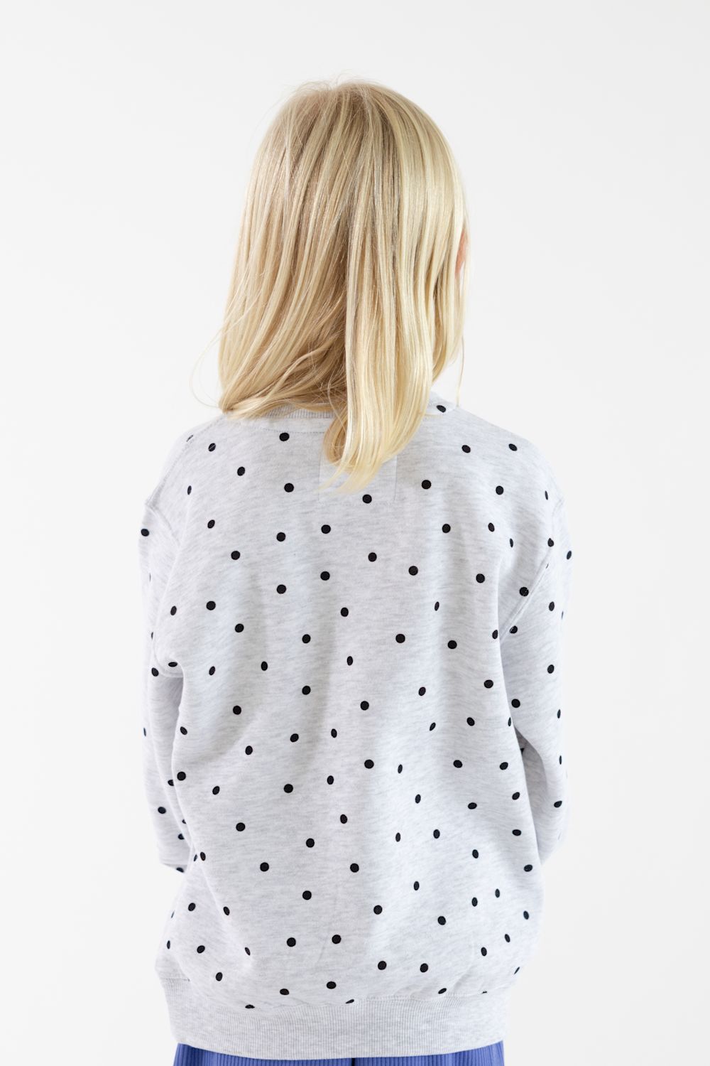 A child viewed from the back wearing a light gray long-sleeve sweatshirt with a black polka dot pattern, set against a plain white background.