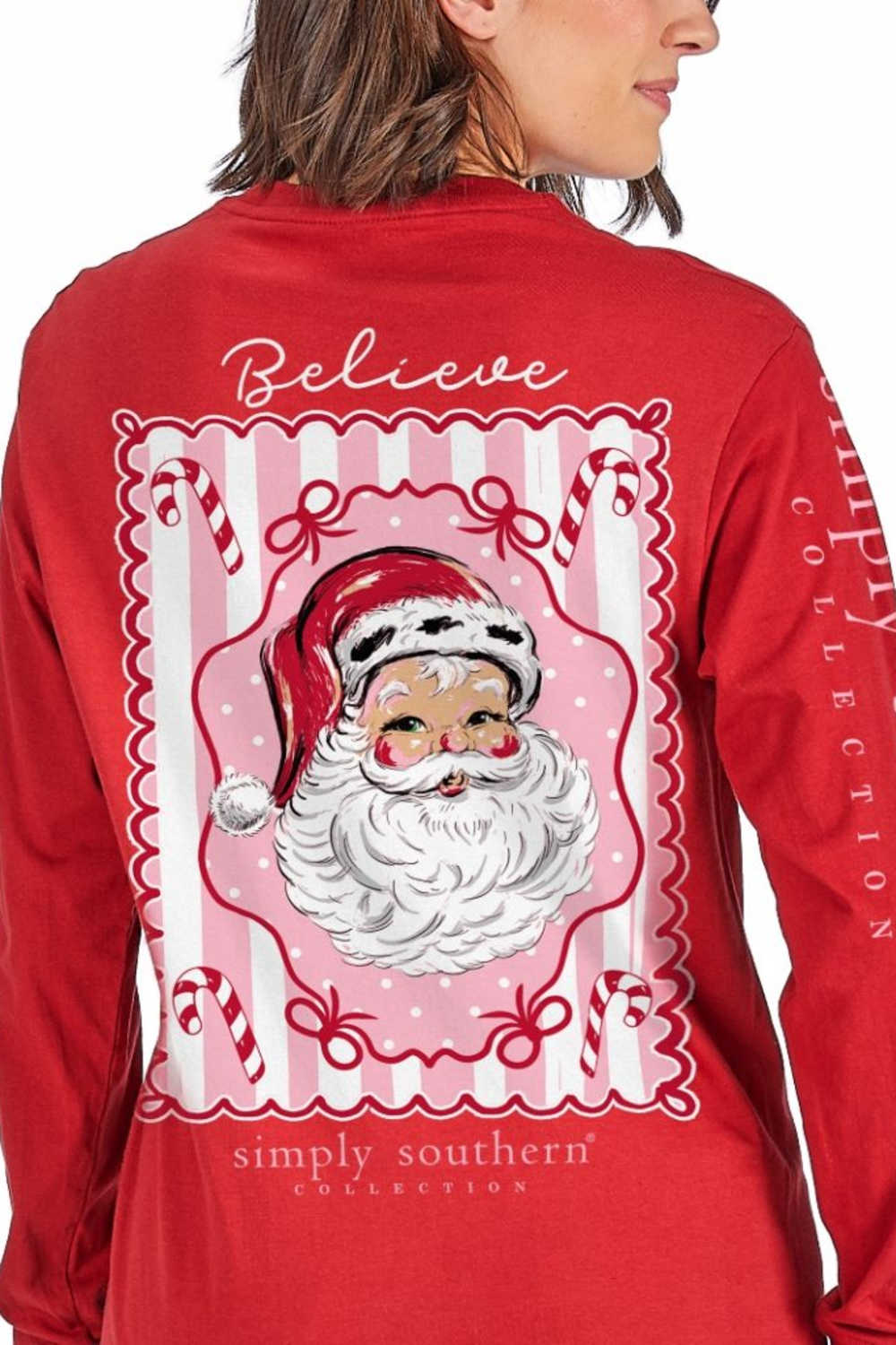 A woman wearing a red long-sleeve shirt, viewed from the back. The shirt features a large graphic print of Santa Claus inside a pink and white scalloped frame, with the words 'Believe' and 'simply southern collection' printed on the back.