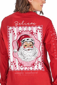 A woman wearing a red long-sleeve shirt, viewed from the back. The shirt features a large graphic print of Santa Claus inside a pink and white scalloped frame, with the words 'Believe' and 'simply southern collection' printed on the back.
