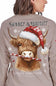 A woman wearing a taupe long-sleeve shirt, viewed from the back. The shirt features a large graphic of a Highland cow wearing a red Santa hat and holding a candy cane, with 'Mooey & Bright' and 'simply southern' collection' printed on the back.