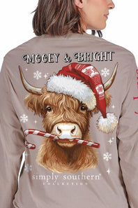A woman wearing a taupe long-sleeve shirt, viewed from the back. The shirt features a large graphic of a Highland cow wearing a red Santa hat and holding a candy cane, with 'Mooey & Bright' and 'simply southern' collection' printed on the back.