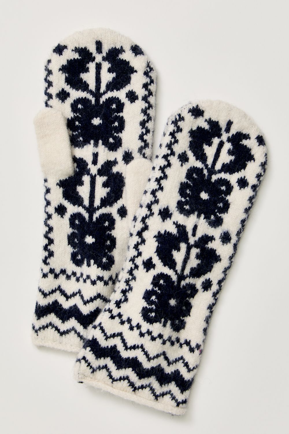A pair of knit fingerless mittens with a dark navy blue Fair Isle pattern on an off-white background, displayed against a light neutral background.