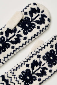 A close-up of a pair of knit mittens with a dark navy blue and off-white Nordic floral pattern, showing the soft fleece lining of one mitten.
