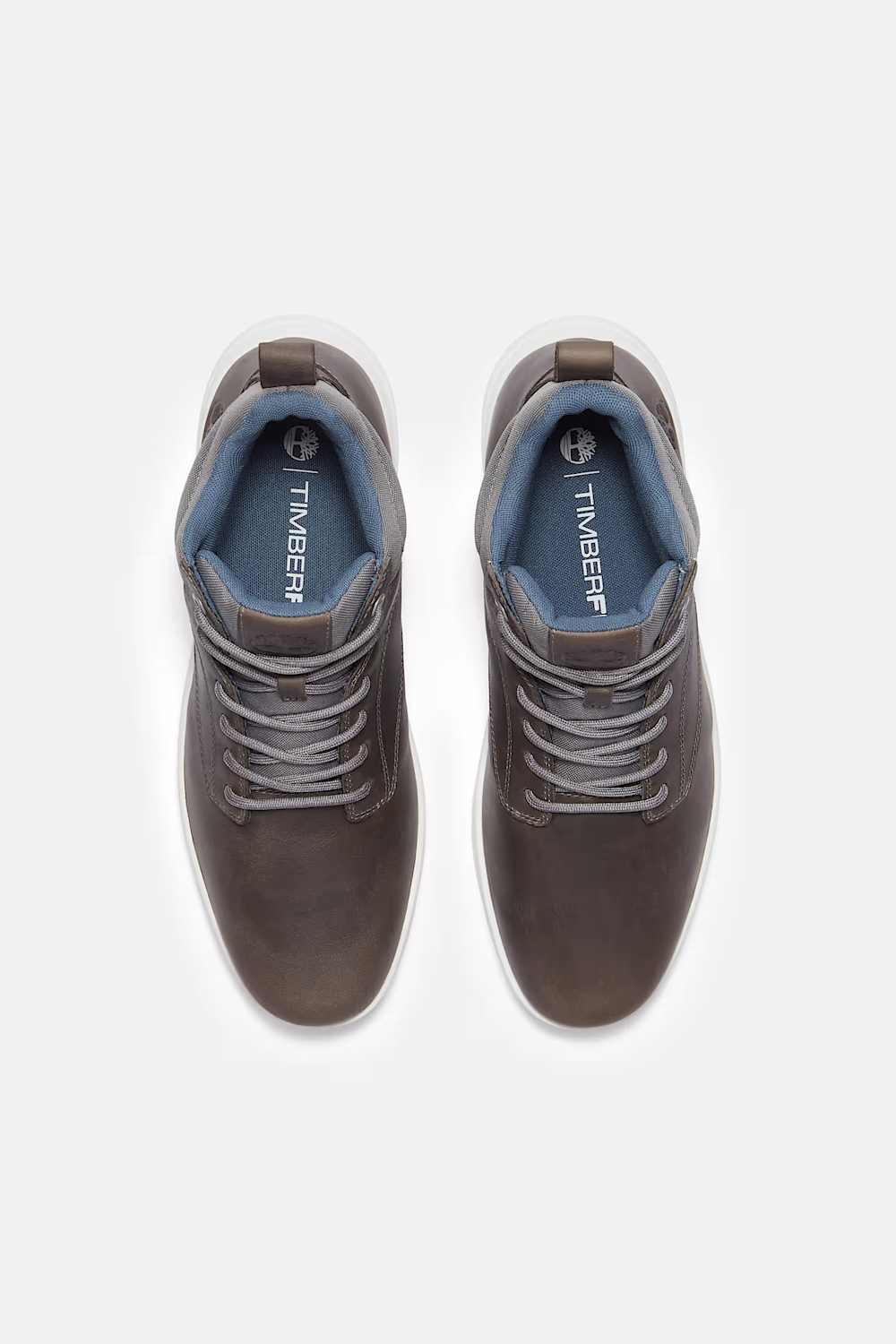 A pair of Timberland mid-top lace-up sneakers in dark brown, viewed from a top-down perspective on a light gray background.