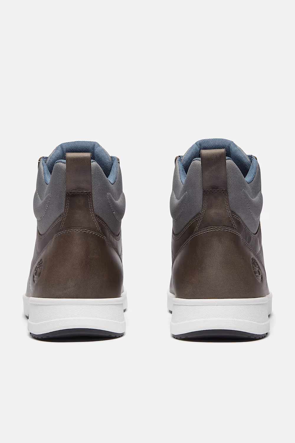 A pair of Timberland mid-top sneakers shown from the back, featuring a dark brown leather upper, gray suede overlays, a light blue lining, and a white midsole.