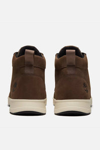 A pair of Timberland mid-top boots shown from the back, featuring brown suede uppers, pull tabs, and a cream-colored midsole.