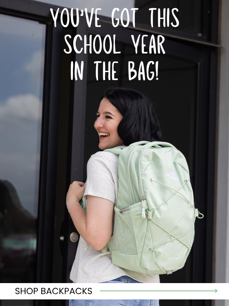 Promotional banner showing a smiling person wearing a mint green backpack outside a building. The text reads, "You've Got This School Year in the Bag!" with a "Shop Backpacks" call-to-action and a right-pointing arrow at the bottom.