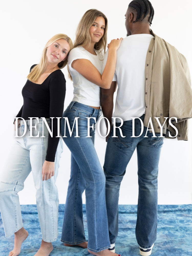 A promotional banner with three models, two female one male, standing in front of a white background and on a blue cloth. From left to right, one female model wears light wash jeans and a basic long sleeve black top. The next female model wears medium wash jeans with a basic short sleeve white top, leaning against the male model. And the back view of a male model wearing dark wash jeans with a white short sleeve t-shirt and tan jacket over his right shoulder. Text reads DENIM FOR DAYS