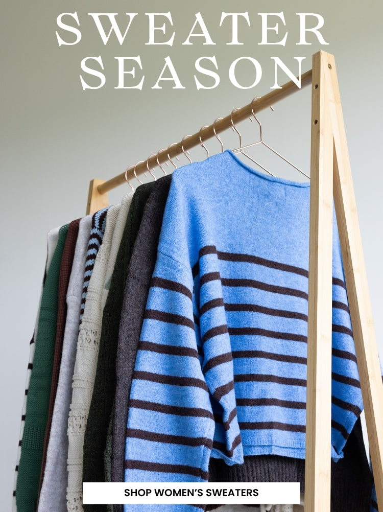 A promotional banner featuring multiple different colored long sleeve sweaters and cardigans hanging on a light colored wooden rack. Text at the top of the image reads SWEATER SEASON plus a white rectangular call to action with SHOP WOMEN'S SWEATERS