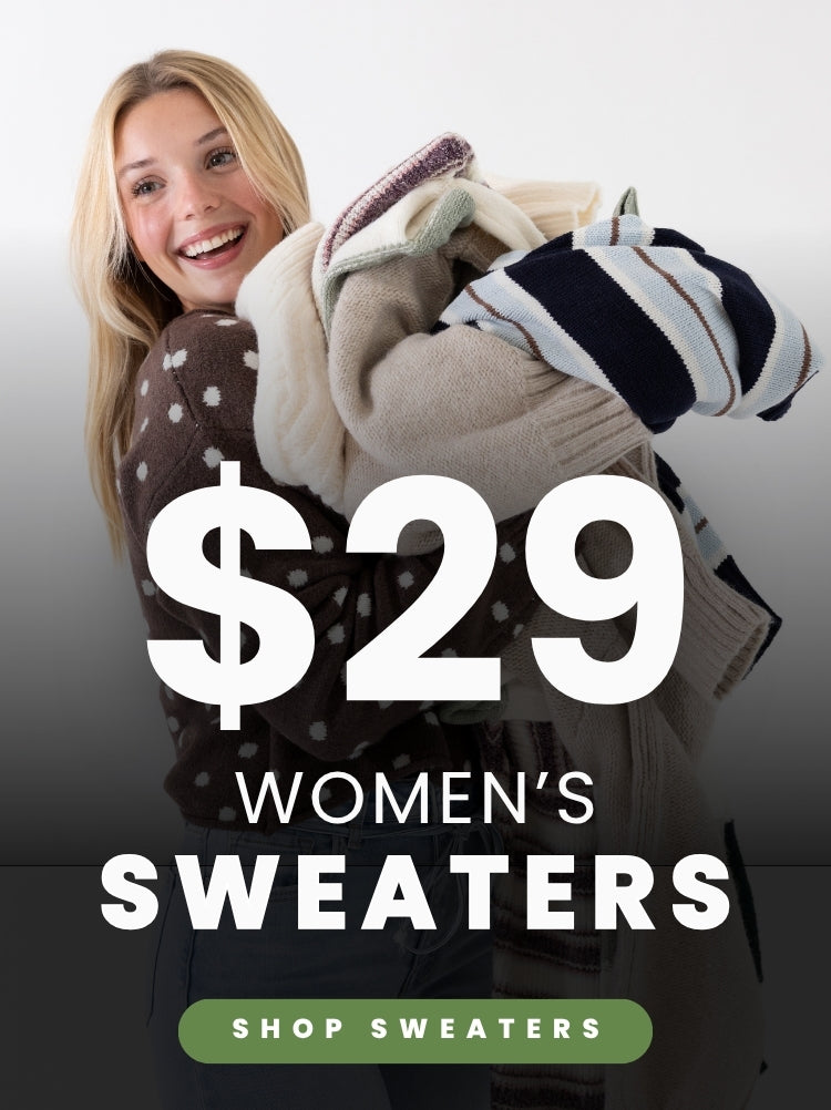A smiling model holds a stack of cozy sweaters while wearing a brown polka-dot sweater and light-wash jeans. Text advertises women’s sweaters for $29 with a green Shop Sweaters button.