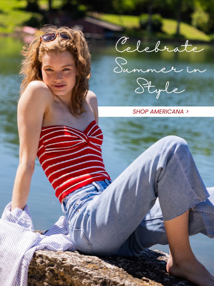 Woman sitting a rocky like surface in front of a lake wearing a strapless red and white striped top and blue jeans with text that reads "Celebrate Summer in Style - Shop Americana"