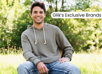 Promotional banner featuring a smiling man wearing a textured gray hoodie and blue jeans outdoors, with text reading “Glik’s Exclusive Brands” over a sunny wooded background.