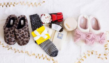 Pair of leopard print slippers, socks with patterned sole, gift box, and candle on a white surface.