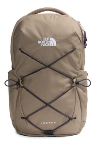 The North Face Jester backpack in a warm khaki-tan color, featuring black bungee cords crisscrossed on the front and a white logo on the upper chest.