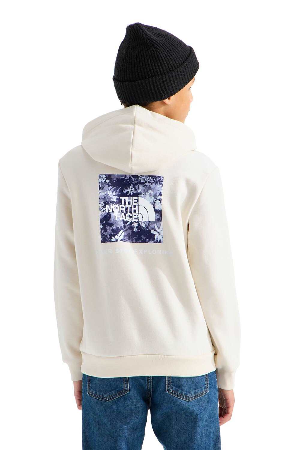 A person shown from the back wearing an off-white hoodie with a large blue and white floral graphic on the back that reads 'THE NORTH FACE'. The person is also wearing a black beanie and blue jeans, photographed against a plain white background.