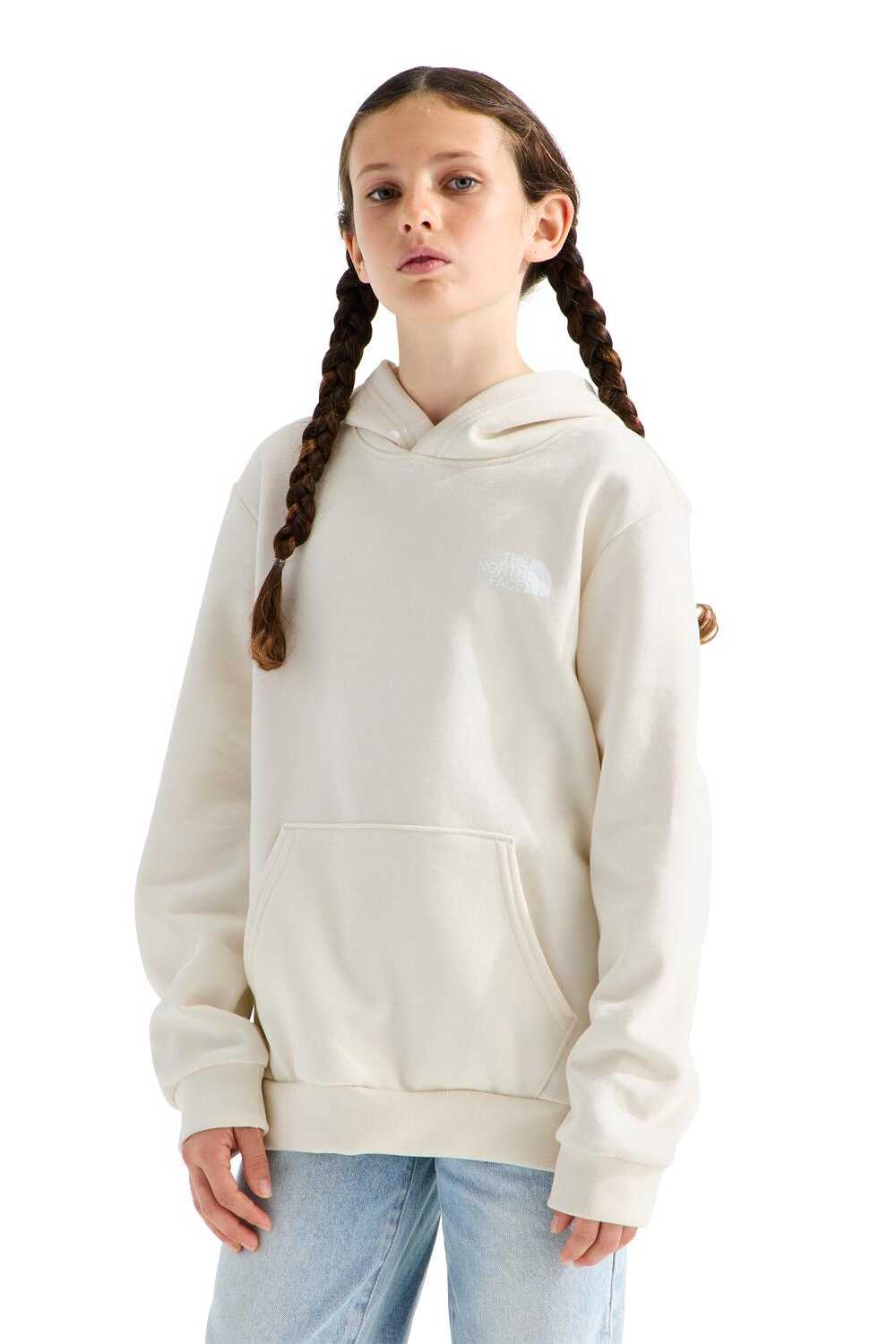 A young girl with braided hair wearing a cream-colored pullover hoodie and light blue jeans, standing against a solid white background.
