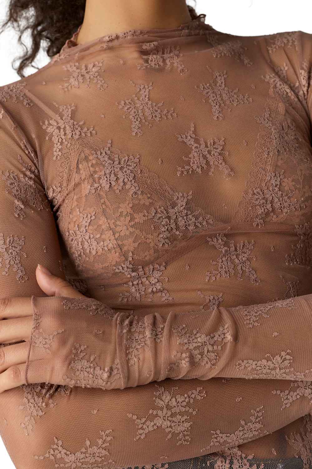 Close-up of a person wearing a sheer taupe-brown long-sleeve top with floral lace applique and a high mock neck.