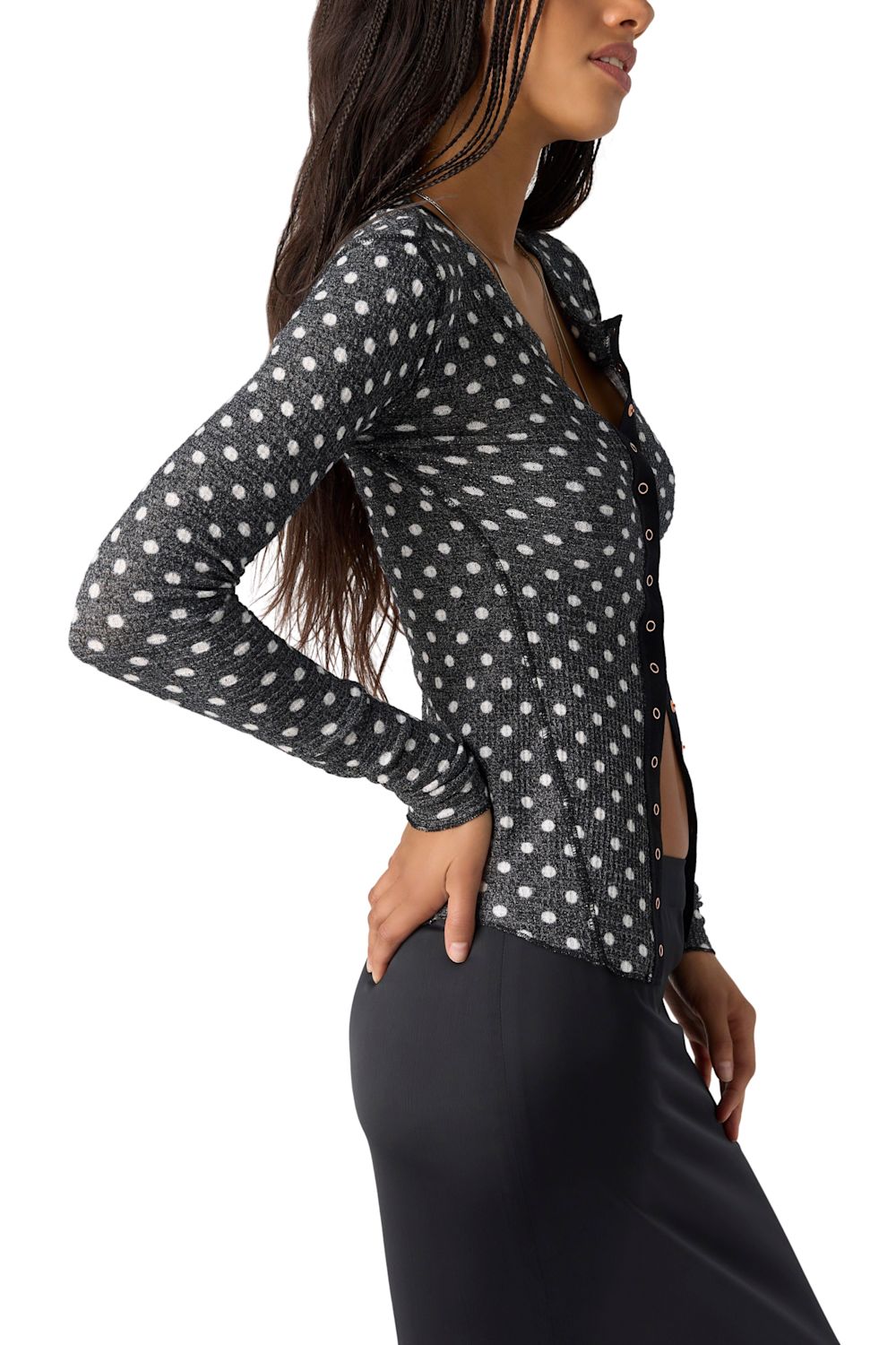 A woman wearing a black long-sleeve cardigan with a white polka-dot pattern and brown buttons, paired with a black skirt, against a plain white background.