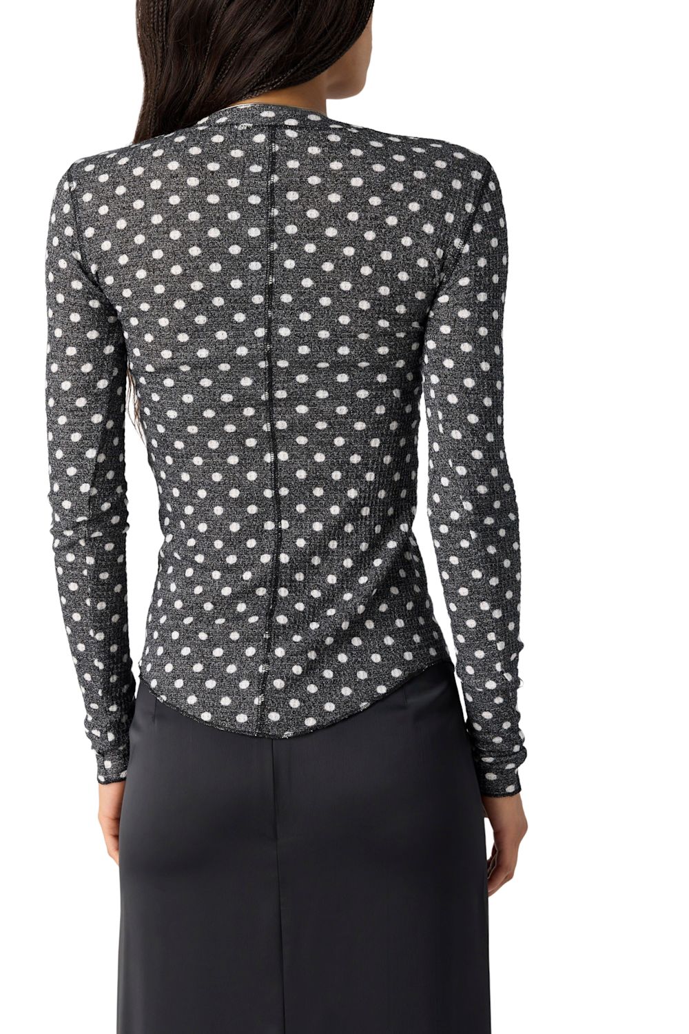 A woman shown from the back wearing a long-sleeve fitted top with a black base and small white floral or dot pattern, paired with a dark skirt against a plain white studio background.