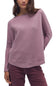 A woman wearing a textured, waffle-knit long-sleeve sweater in a dusty mauve-pink color, paired with dark burgundy pants, against a plain white background.